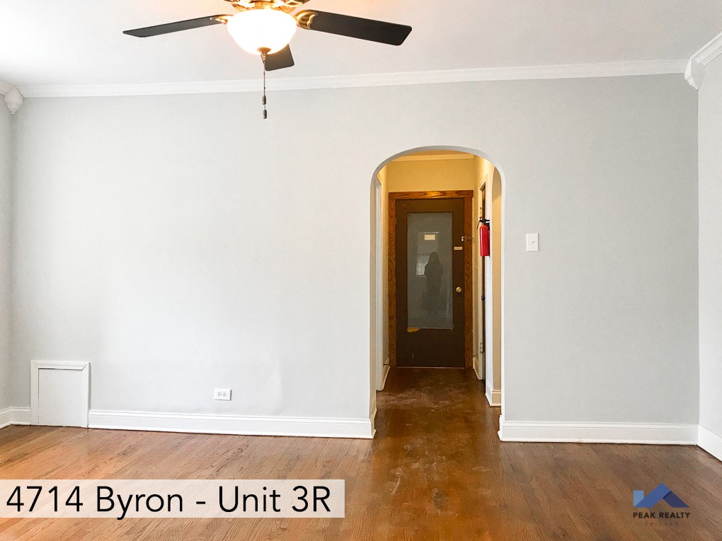an empty room with white walls and a ceiling fan and a door to a hallway