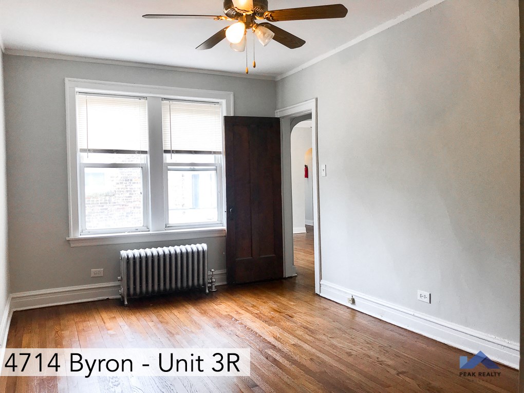 a room with wood floors and a ceiling fan and two windows
