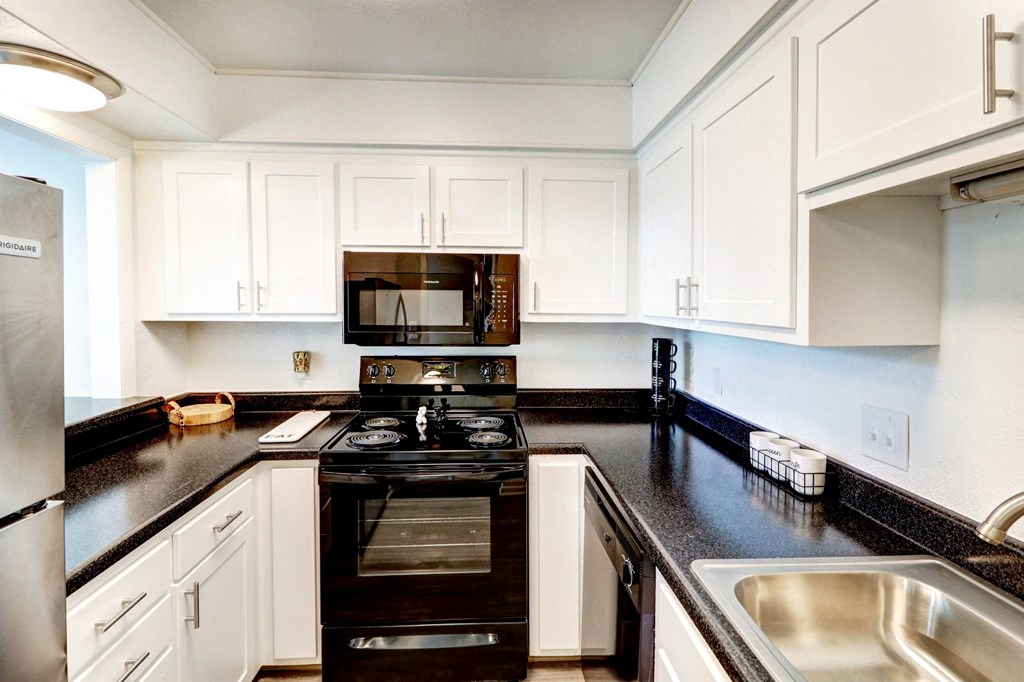 a kitchen with white cabinets and black counter tops and a black stove top oven