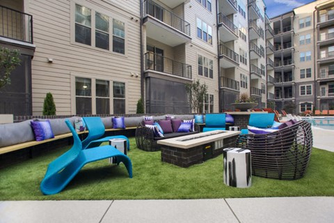 an outdoor lounge area with couches and tables in front of an apartment building