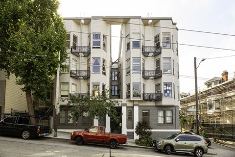 A red truck is parked in front of a white building with black railings.