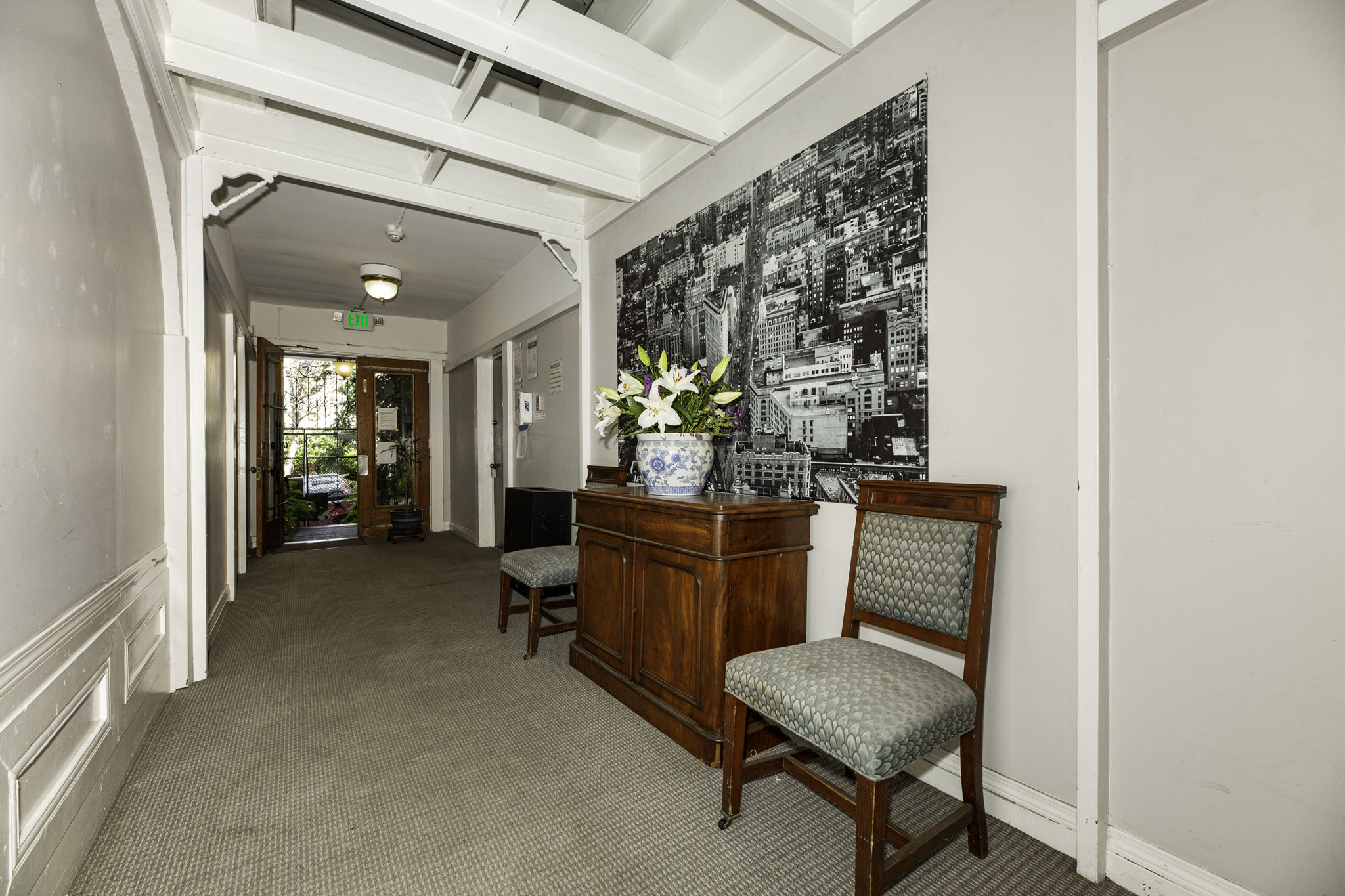 A hallway with a chair and a cabinet with a vase of flowers on top.