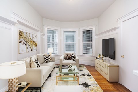 A living room with a white couch, a glass coffee table, and a painting on the wall.