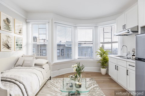 A white bedroom with a bed, a plant, and a glass coffee table.