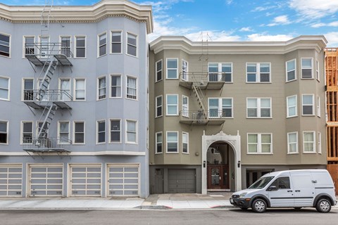 A white van is parked in front of a tan building.