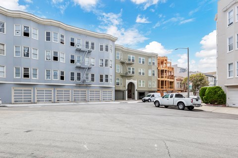 A parking lot with a white truck and a grey building with a fire escape.