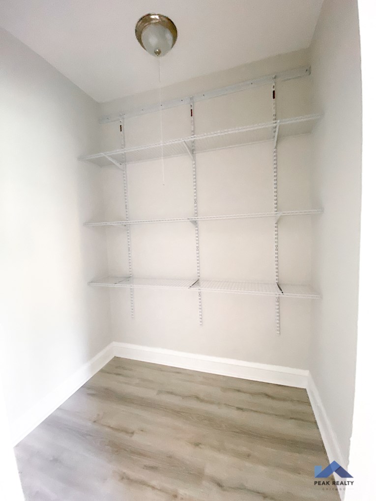 a walk in closet with white shelving and wood flooring