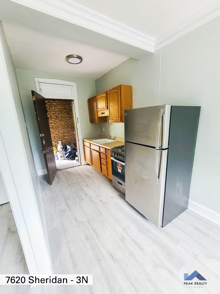 an empty kitchen with a stainless steel refrigerator and wooden cabinets