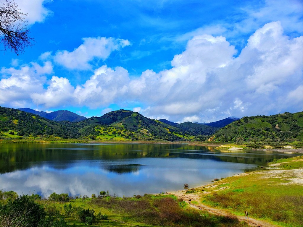 a lake with mountains in the background and a blue sky with clouds
