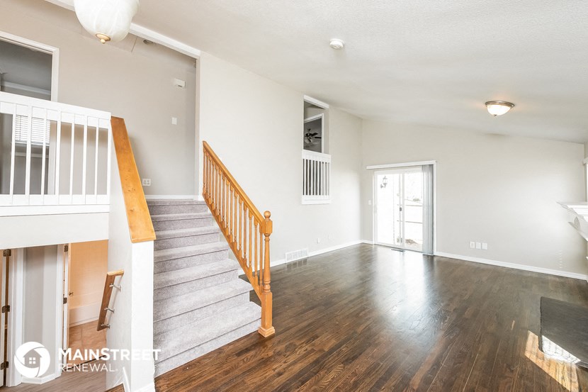 the living room and entryway of a house with wood flooring and a staircase