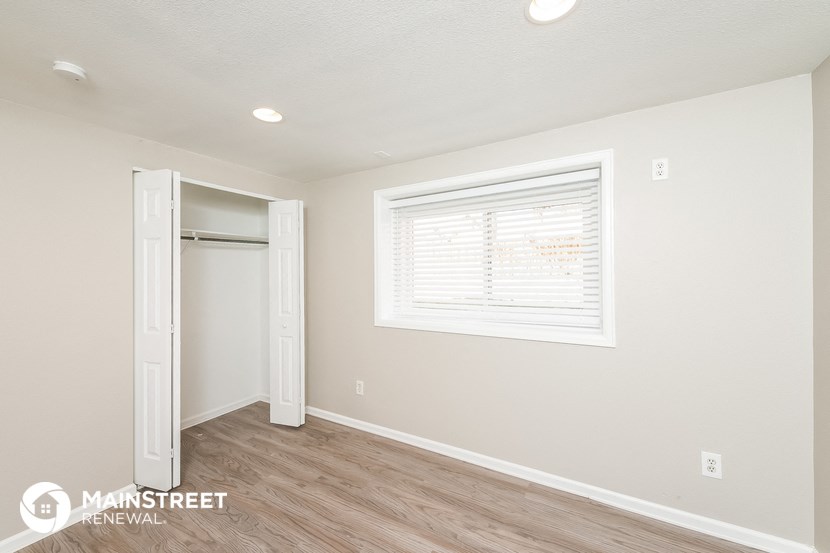 the living room of an apartment with a door to the closet and a window
