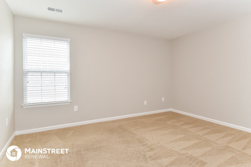 the bedroom of an apartment with beige carpet and a window