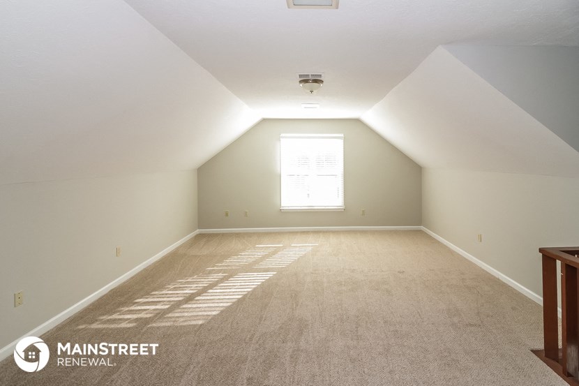 the attic of a home with carpet and a window