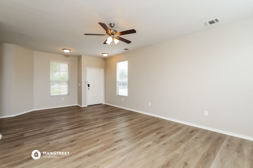 the spacious living room with hardwood floors and a ceiling fan