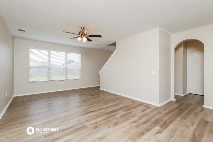 the spacious living room with hardwood flooring and a ceiling fan