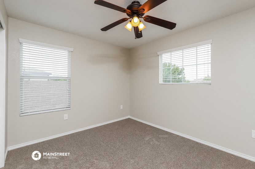 the bedroom has a ceiling fan and two windows