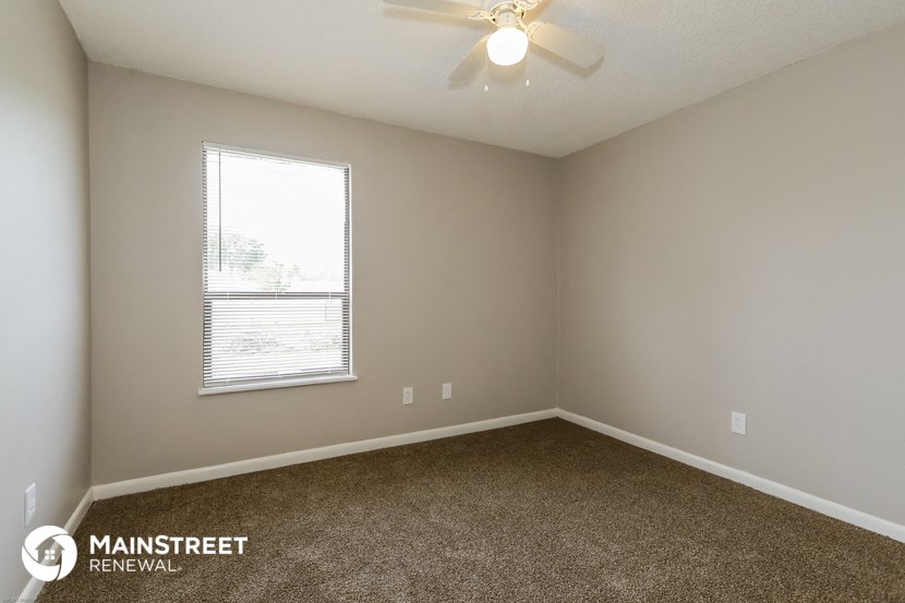 the spacious bedroom with carpeted flooring and a ceiling fan
