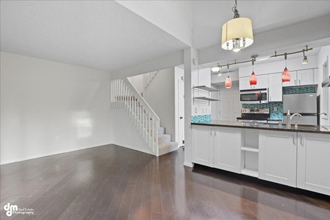 A spacious kitchen with white cabinets and a staircase in the background.