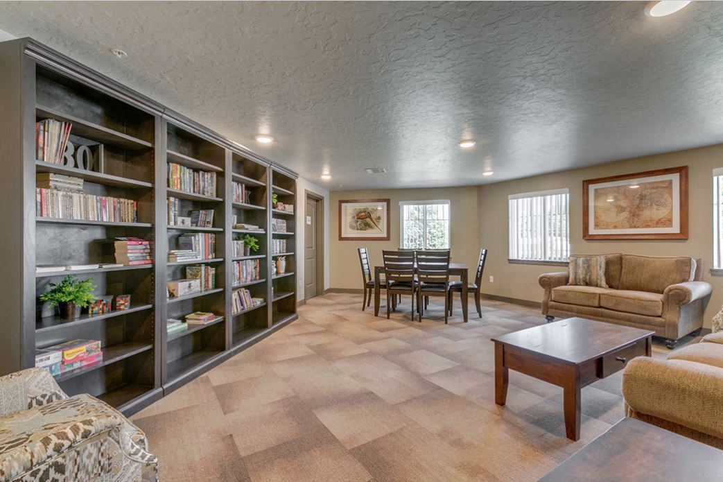 Image of book shelves with books, couches, coffee table, and kitchen table with chairs along with windows