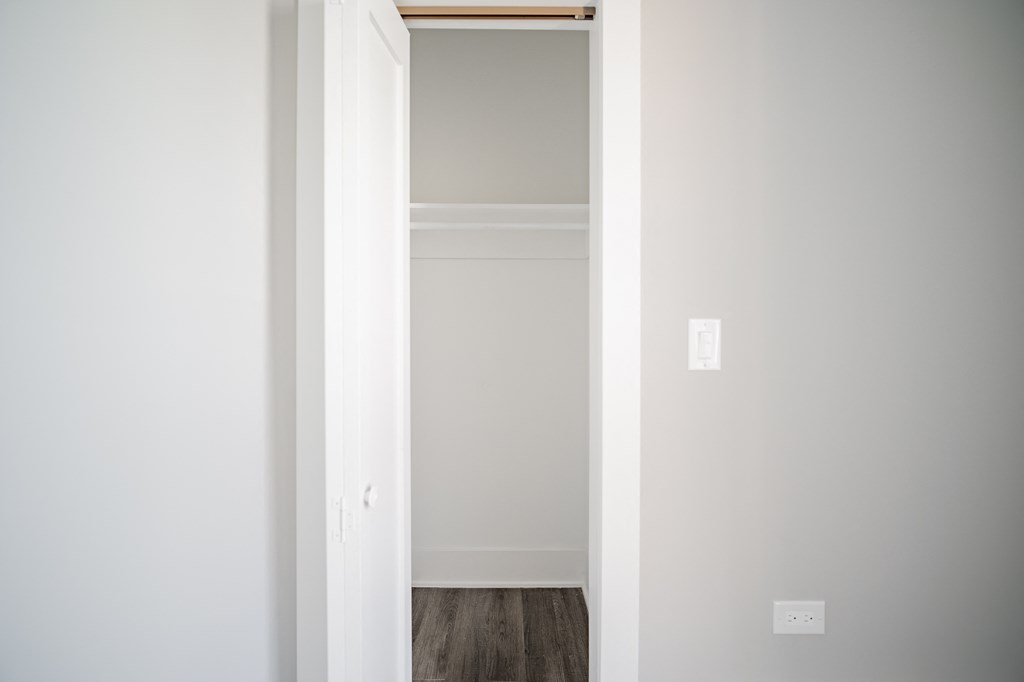 a bedroom with white walls and wood floors and a closet