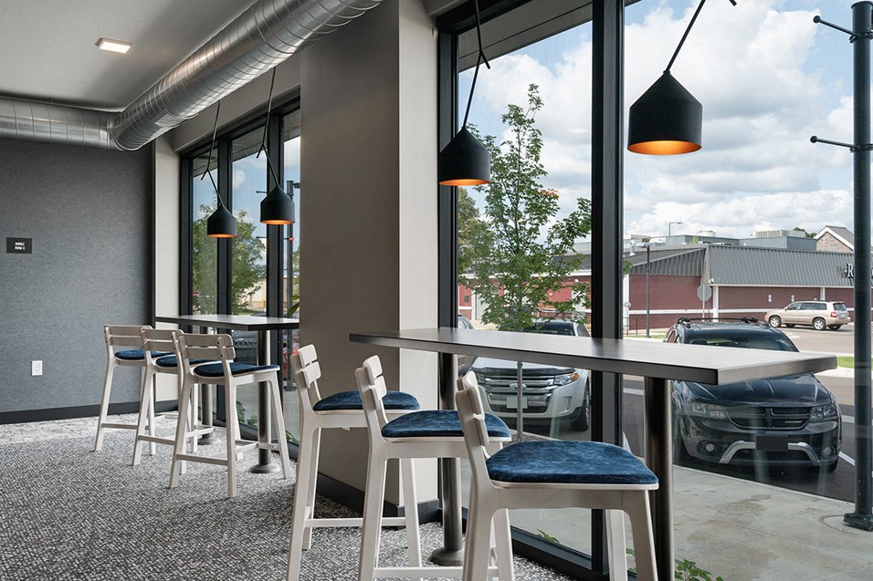 a seating area with tables and chairs in front of a window with cars parked outside