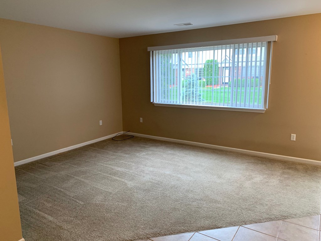 an empty living room with a window and carpet