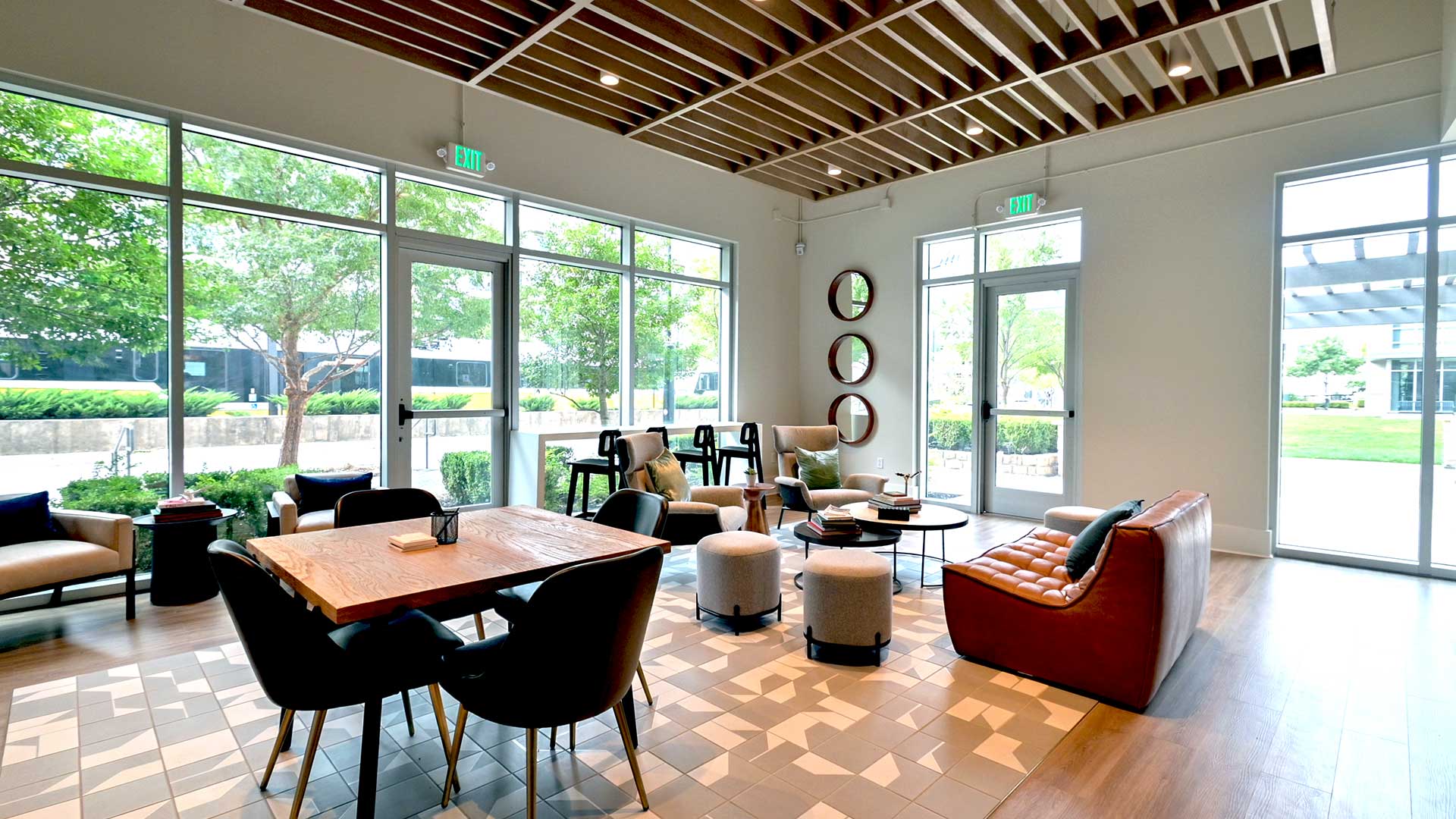 A table and chairs is on the left with a couch and lounge chairs further back on the right. The far walls are all windows with other seating in front of them.