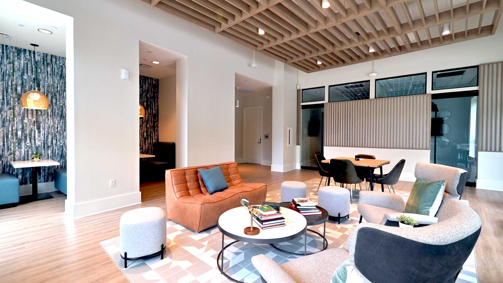 Lounge chairs and an armless couch are in the middle with a table and chairs behind to the right. There are private booths built into the wall on the left and private offices ahead and to the right.