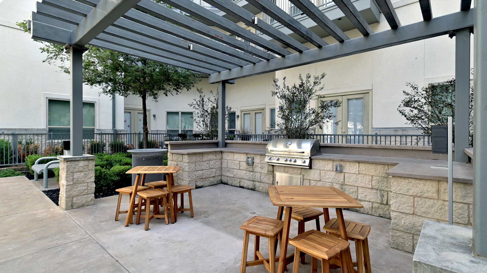 Two sets of wooden tables and stools sit before a built-in grill in the courtyard.