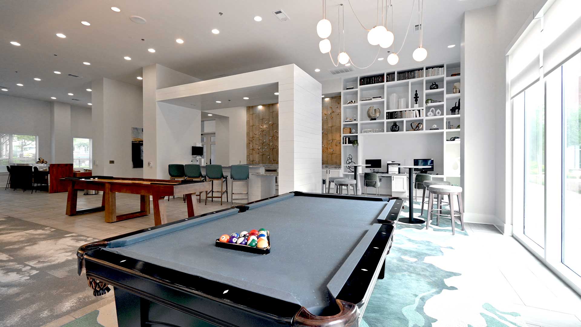 Looking across a blue felt pool table in the lounge. There are high top tables, two computer stations and bar behind.