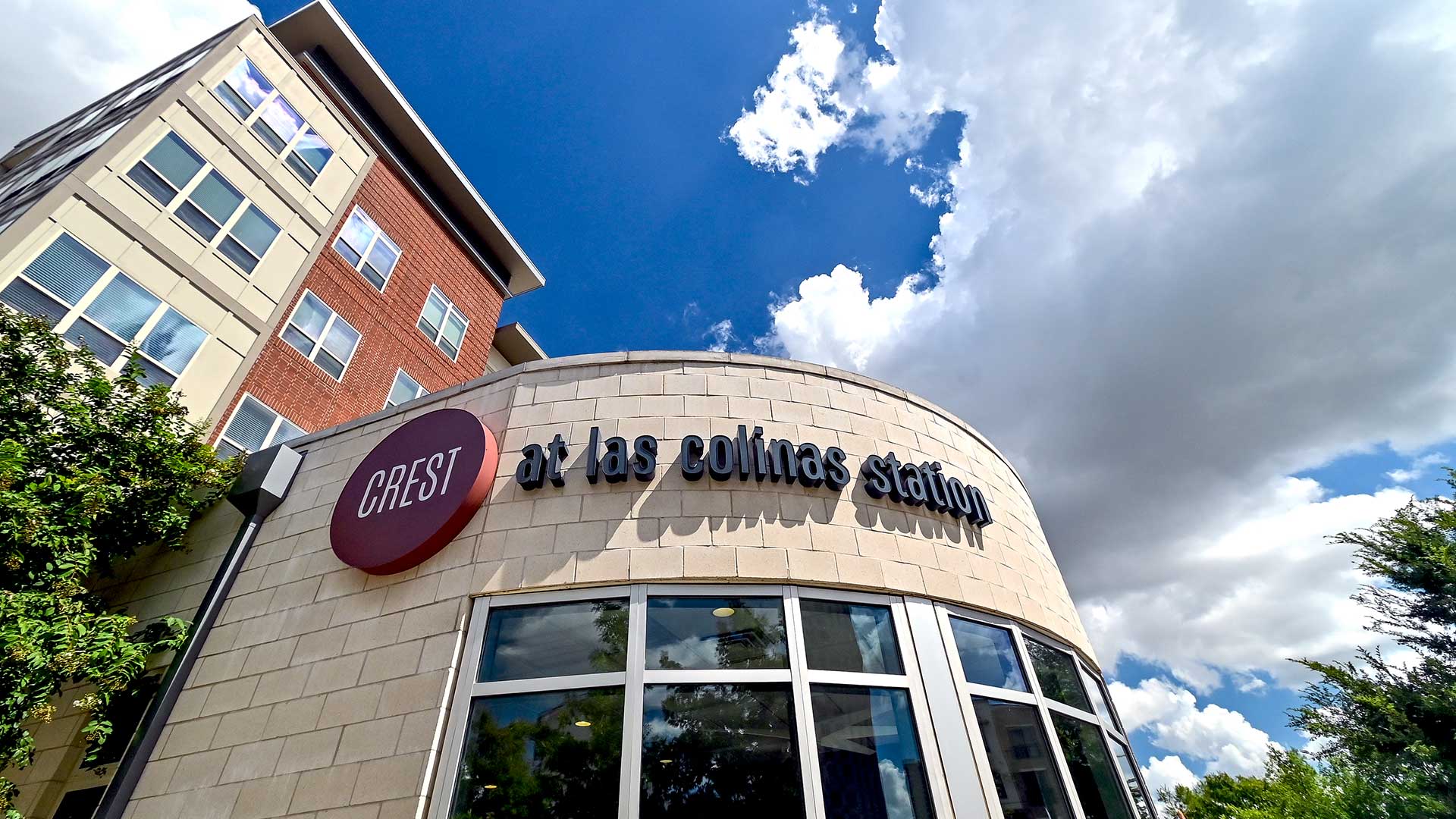 Looking up at the Crest at Las Colinas Station sign on the curved building front above a set of windows.