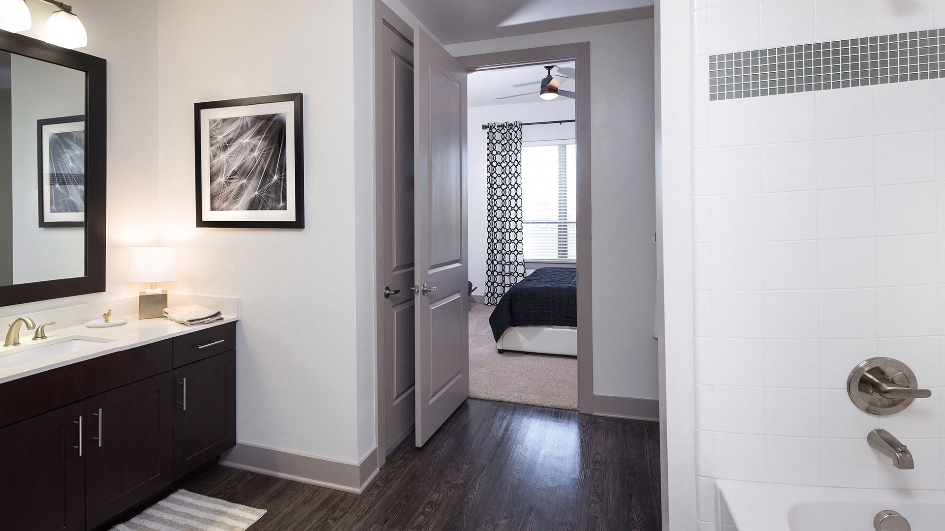 Standing in a residence bathroom looking back out into the bedroom. To the left is a vanity and to the right in the bathtub.