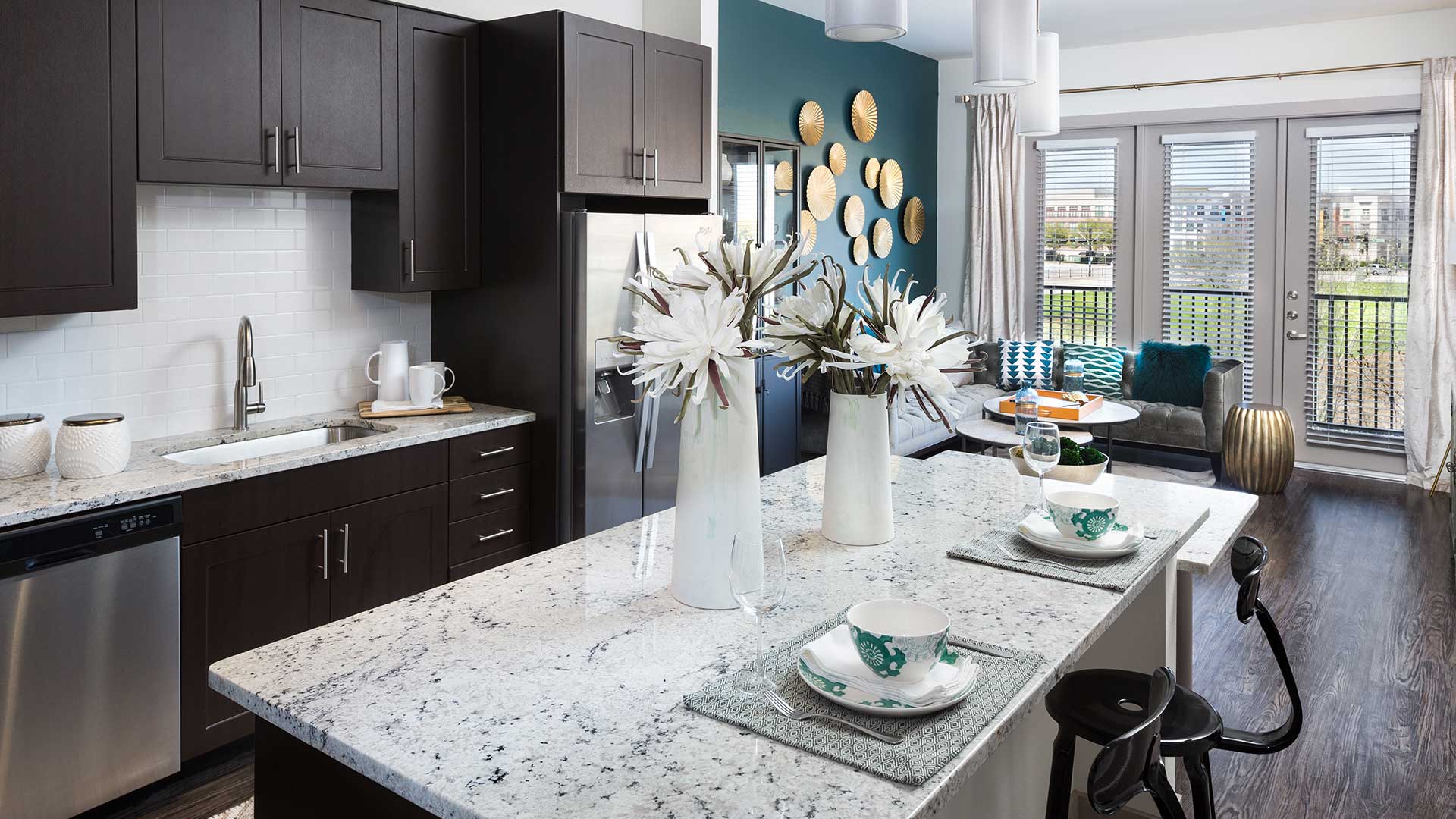 Looking along the kitchen island in a residence at Crest at Las Colinas Station. The kitchen runs along the left wall with ebony cabinets and stainless steel appliances.