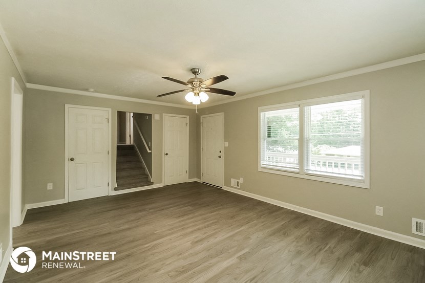 the living room of a home with a ceiling fan and a door into a hallway