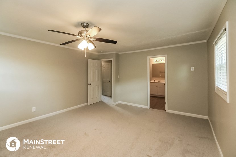 an empty living room with a ceiling fan and a door to a bathroom