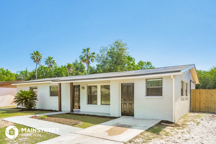 a small white house with a driveway and palm trees