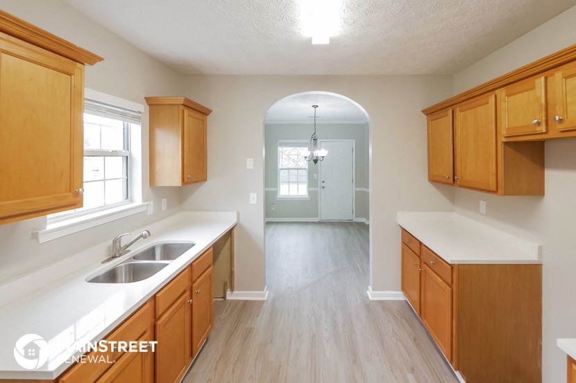 an empty kitchen with wooden cabinets and white countertops and a hallway with a sink