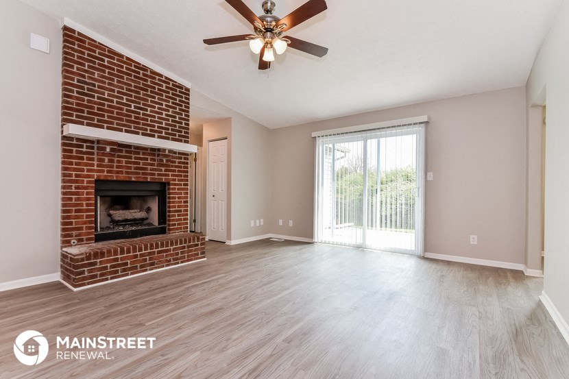an empty living room with a brick fireplace and a ceiling fan