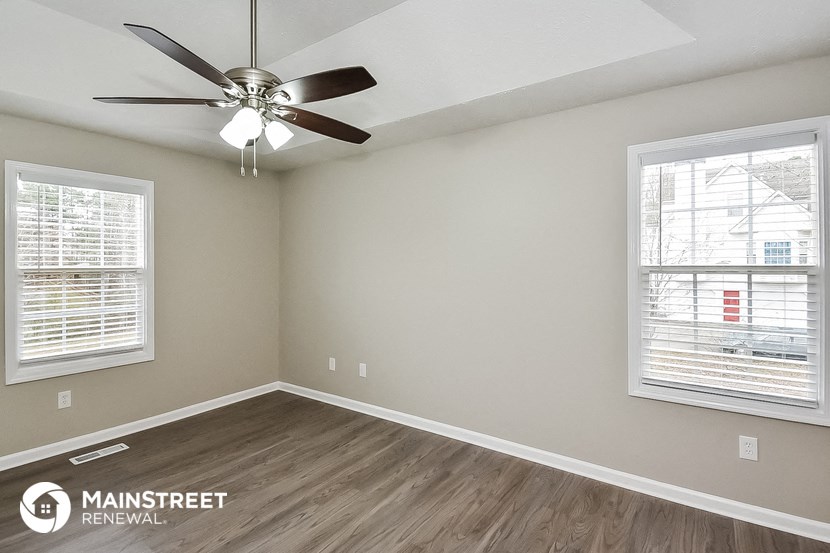 the spacious living room has a ceiling fan and two windows
