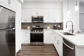 furnished white kitchen with stainless steel appliances Apartments for Rent in Montclair CA - Spacious Kitchen Featuring Plenty of Storage and Counter Space and Convenient Amenities Such as Stove, Microwave, Fridge, and Dishwasher - Photo Gallery 3
