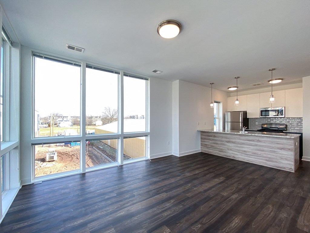 an empty living room with a large window and a kitchen