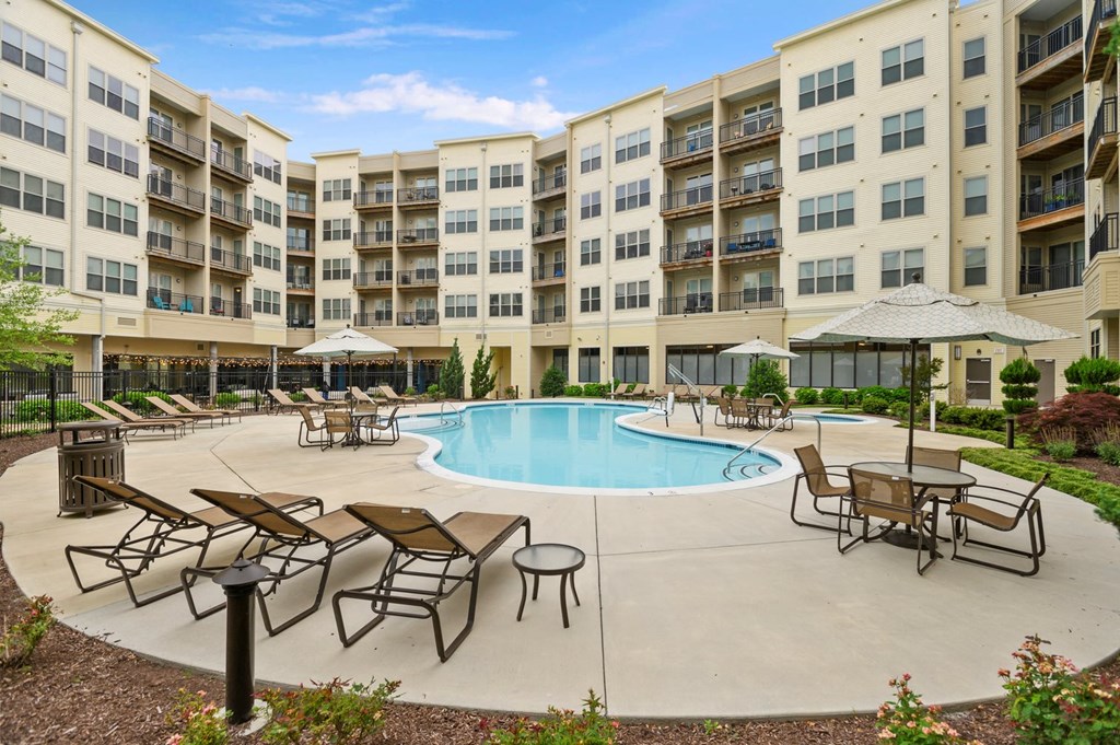 a large swimming pool with patio furniture in front of an apartment building