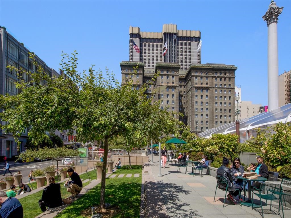 people sitting at tables in a park in front of a tall building
