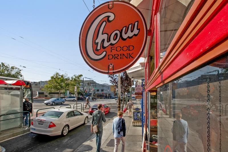 people walking on the sidewalk in front of a chow food drink sign