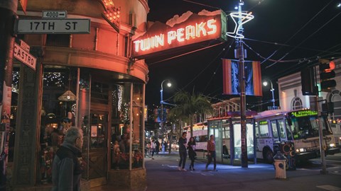 people walking on a street at night in front of a building with a neon sign
