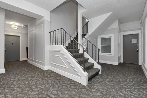 A hallway with a staircase and a patterned carpet.