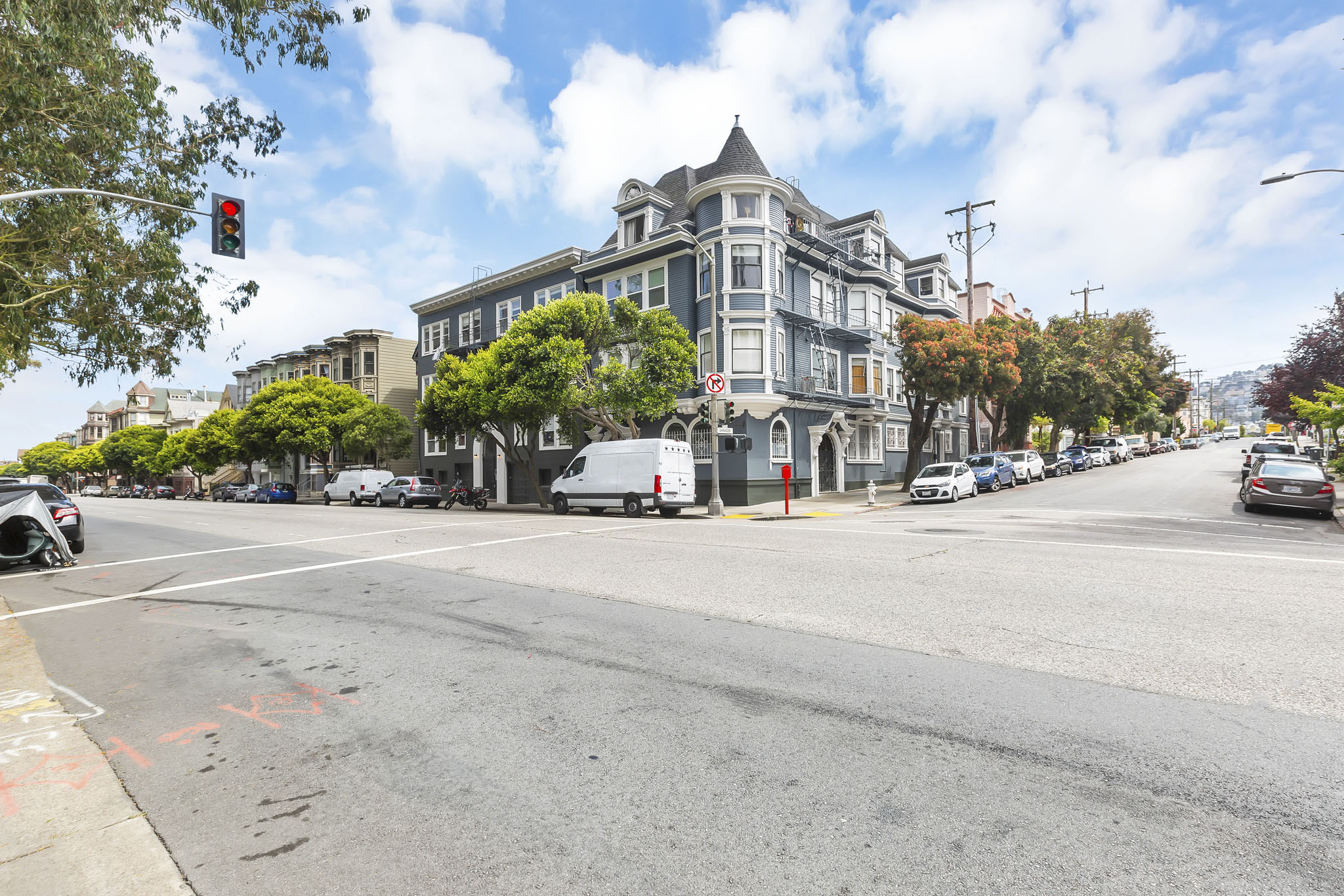A street view with a large building on the corner and cars parked on the side of the road.