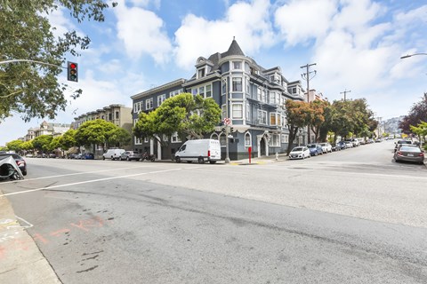 A street view with a large building on the corner and cars parked on the side of the road.