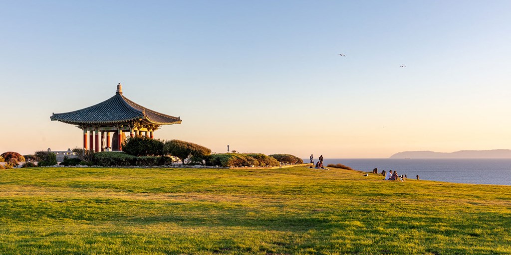 people walking around a pagoda on a hill near the ocean