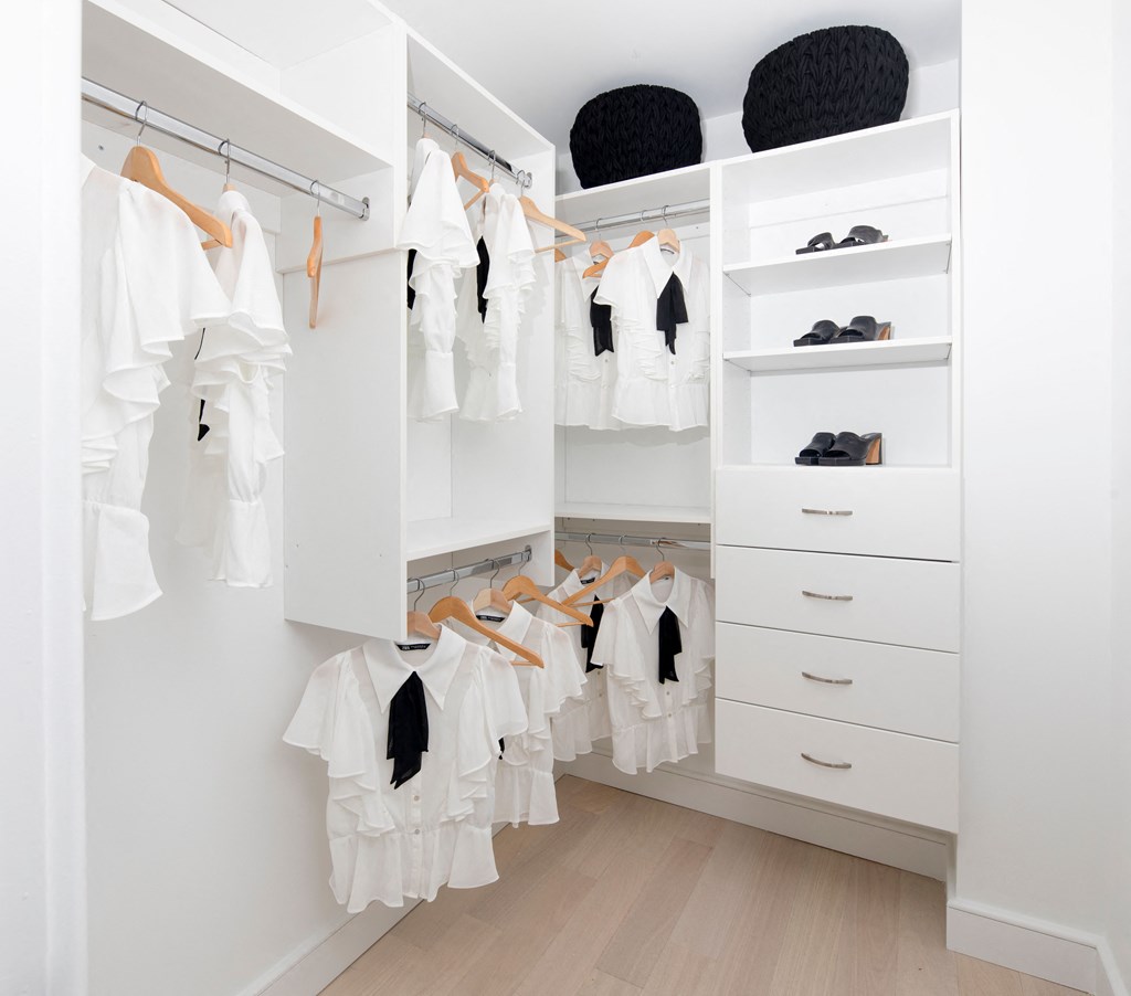 a closet with white cabinets and a white wardrobe with clothes hanging